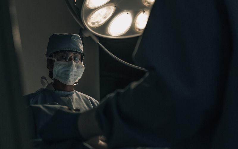 Cirujano con cubrebocas y gorro bajo la lámpara del quirófano