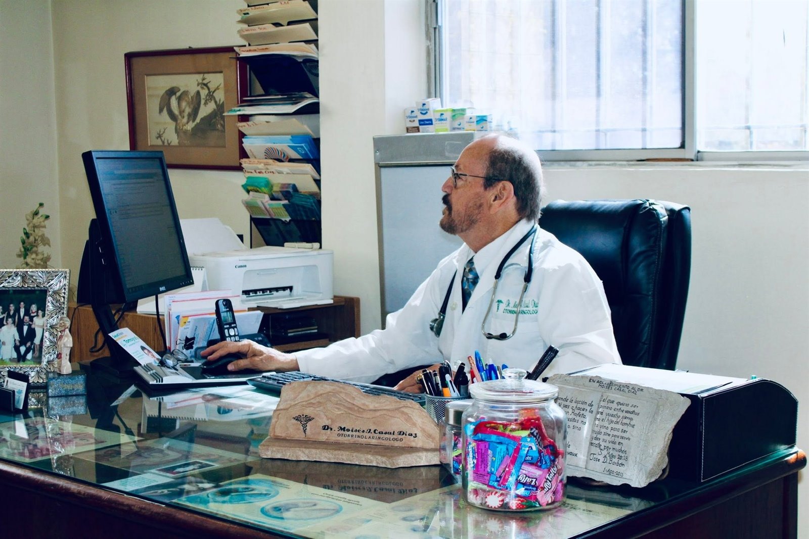 El Dr. Moisés Casal Díaz con bata trabajando en su escritorio del consultorio