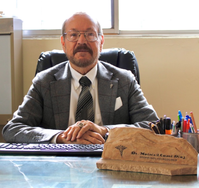 Retrato del Dr. Moisés Casal Díaz en su escritorio, junto a su placa de otorrinolaringólogo