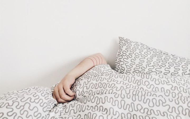 Brazo asomando bajo el edredón en una cama deshecha